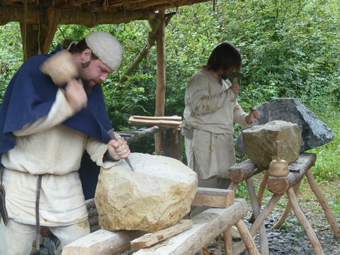 2 Männer in mittelalterlicher Gewandung bearbeiten Steine mit Hammer und Meißel