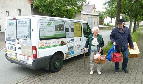 Zwei Senioren mit Einkaufskörben vor einem Kleinbus