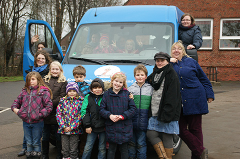 Kinder, Jugendliche und Erwachsene stehen vor und neben einem blauen Kleinbus und sitzen auch darin.